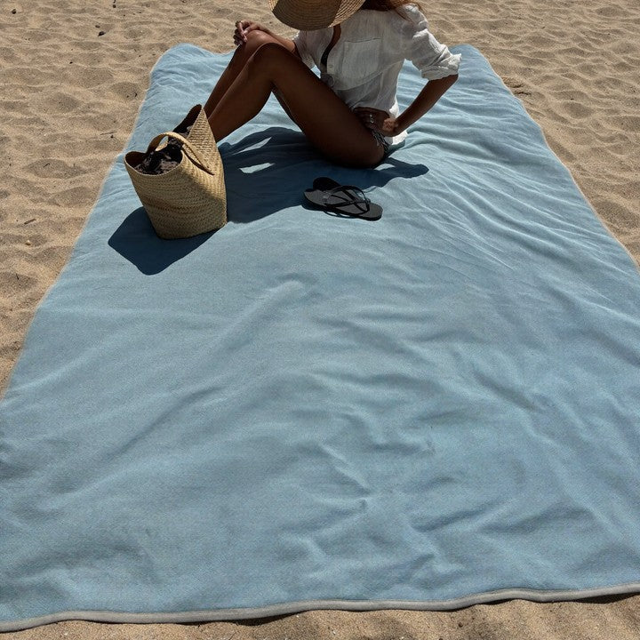 Le drap ZéroSable déplié sur le sable, une personne assise dessus